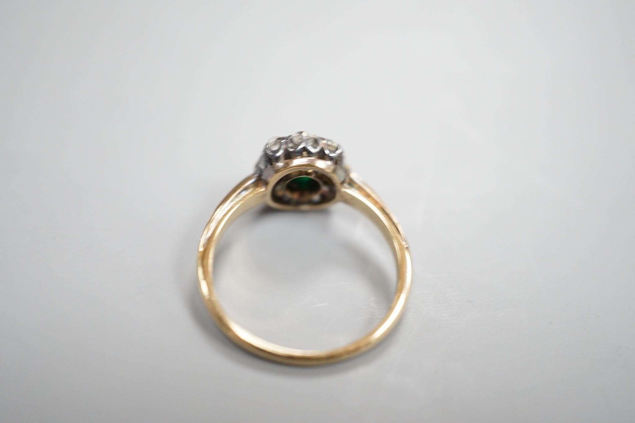 A yellow metal, emerald and diamond set oval cluster ring, size M/N, gross weight 3.1 grams.